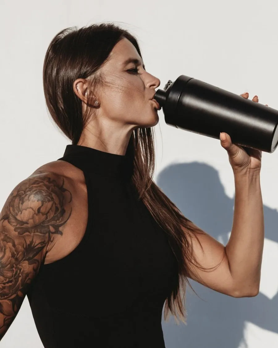 Woman drinking a protein shake from a black shaker bottle after a workout