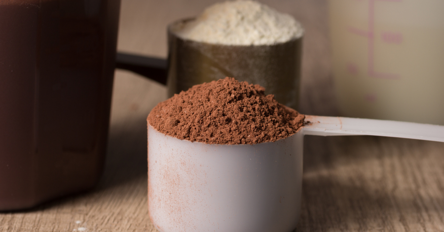 Scoop of beef protein powder beside a glass of protein shake on a kitchen counter