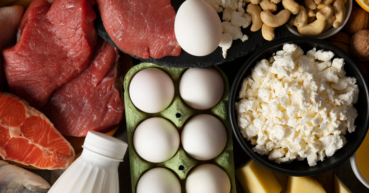 Variety of raw grass-fed meats, eggs, butter, and organ cuts arranged on a butcher paper-lined counter