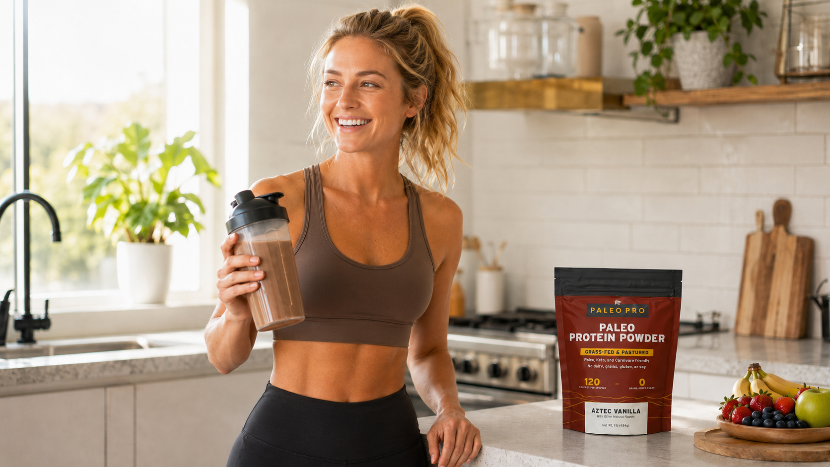 Woman in workout clothes holding a protein shake in a shaker bottle in a sunlit kitchen