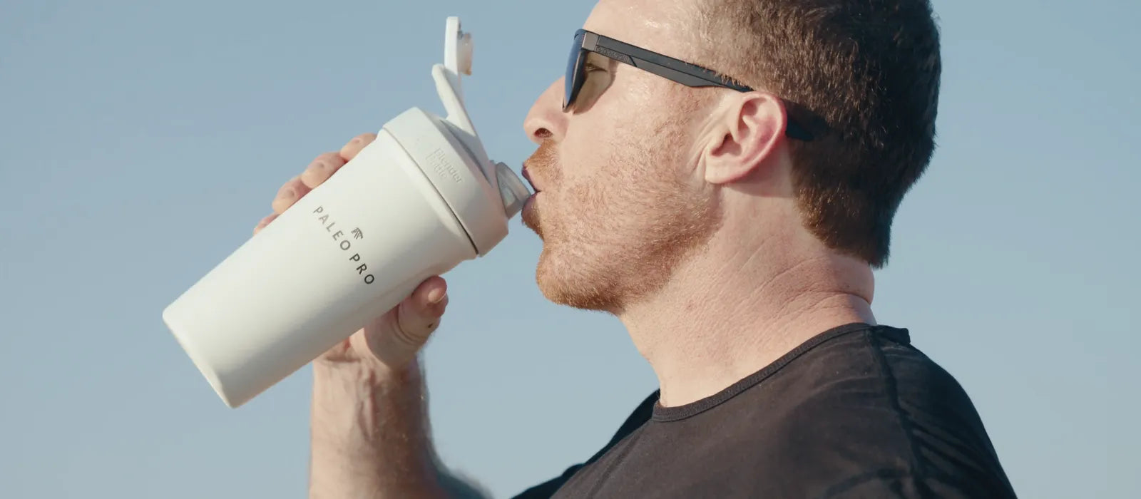 Man drinking a Paleo Pro shake from a white shaker bottle outdoors